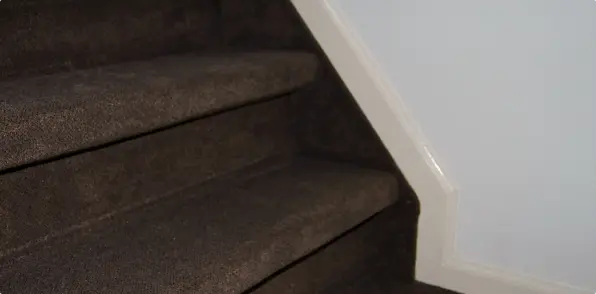 Foto van een bruin gestoffeerde trap met een witte plinten